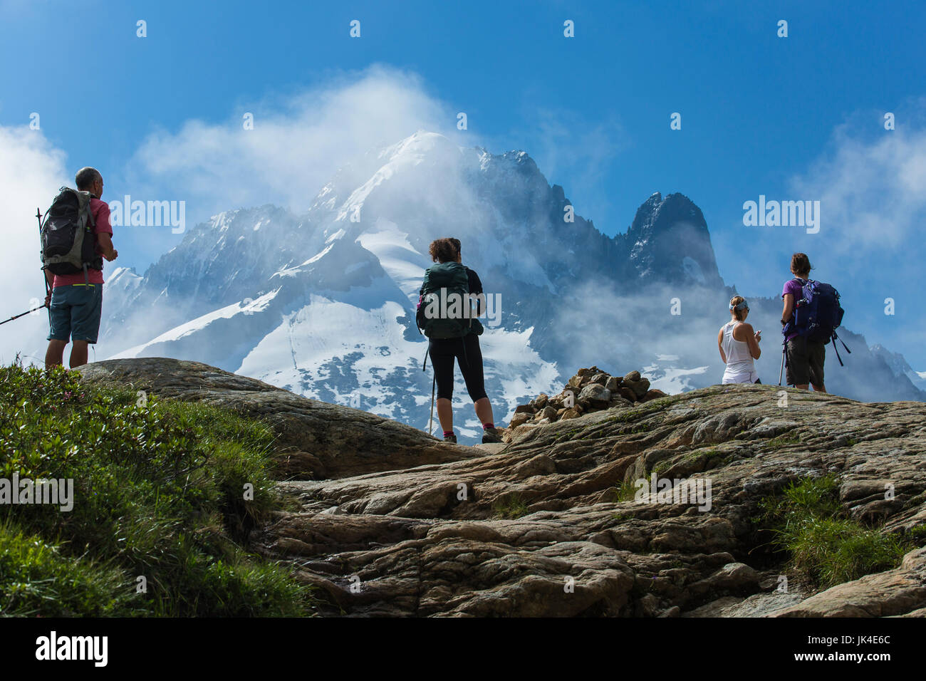 Trois randonneurs se tenir sur une falaise dans les Alpes françaises au-dessus de Chamonix. Tall, pics couverts de neige et nuages en arrière-plan. Banque D'Images