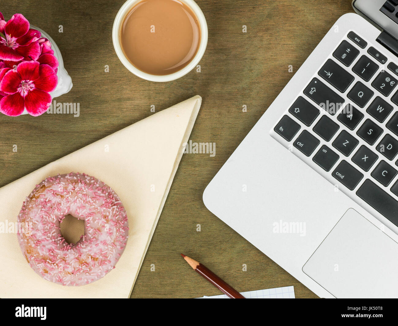 Beignet glacé à un poste de travail avec une tasse de thé à l'encontre d'un bureau en bois en difficulté Banque D'Images