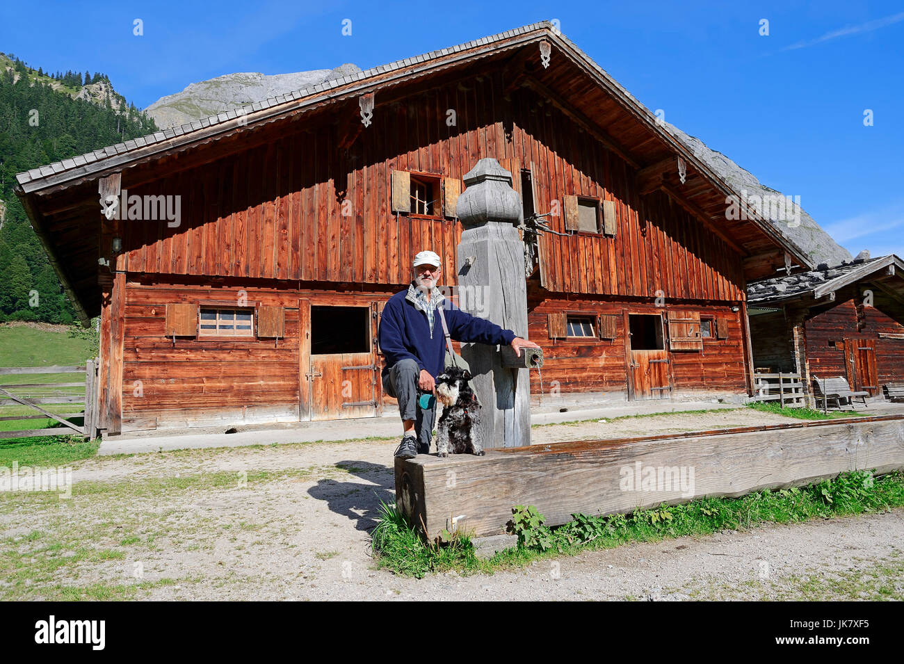 Homme avec Schnauzer nain, noir-argent, à fontaine en bois et chalet de montagne, Grosser Ahornboden, park Karwendel, fra vallée, Tyrol, Autriche Banque D'Images
