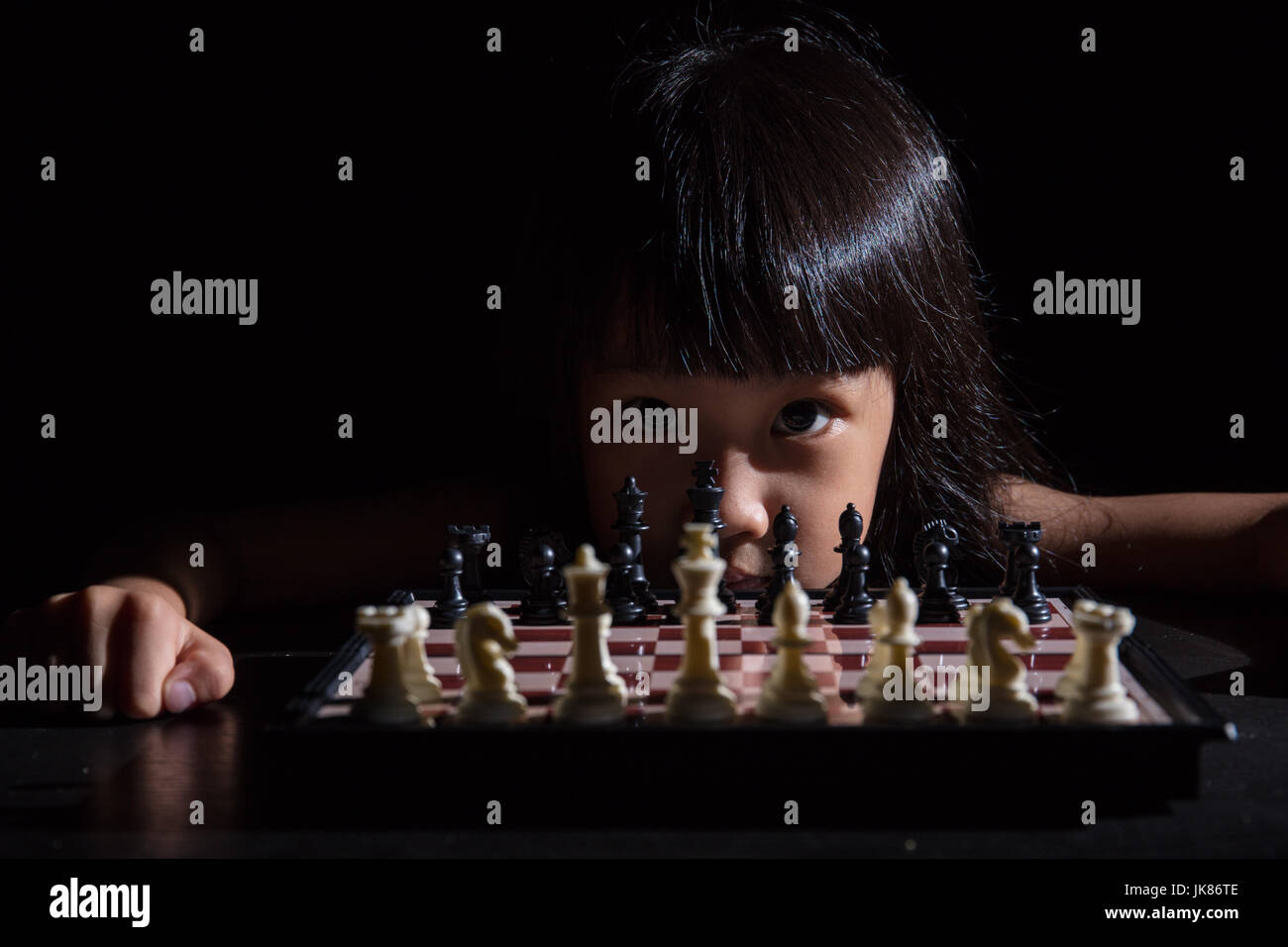 Petite fille asiatique chinois jouant aux échecs dans l'arrière-plan noir isolé Banque D'Images
