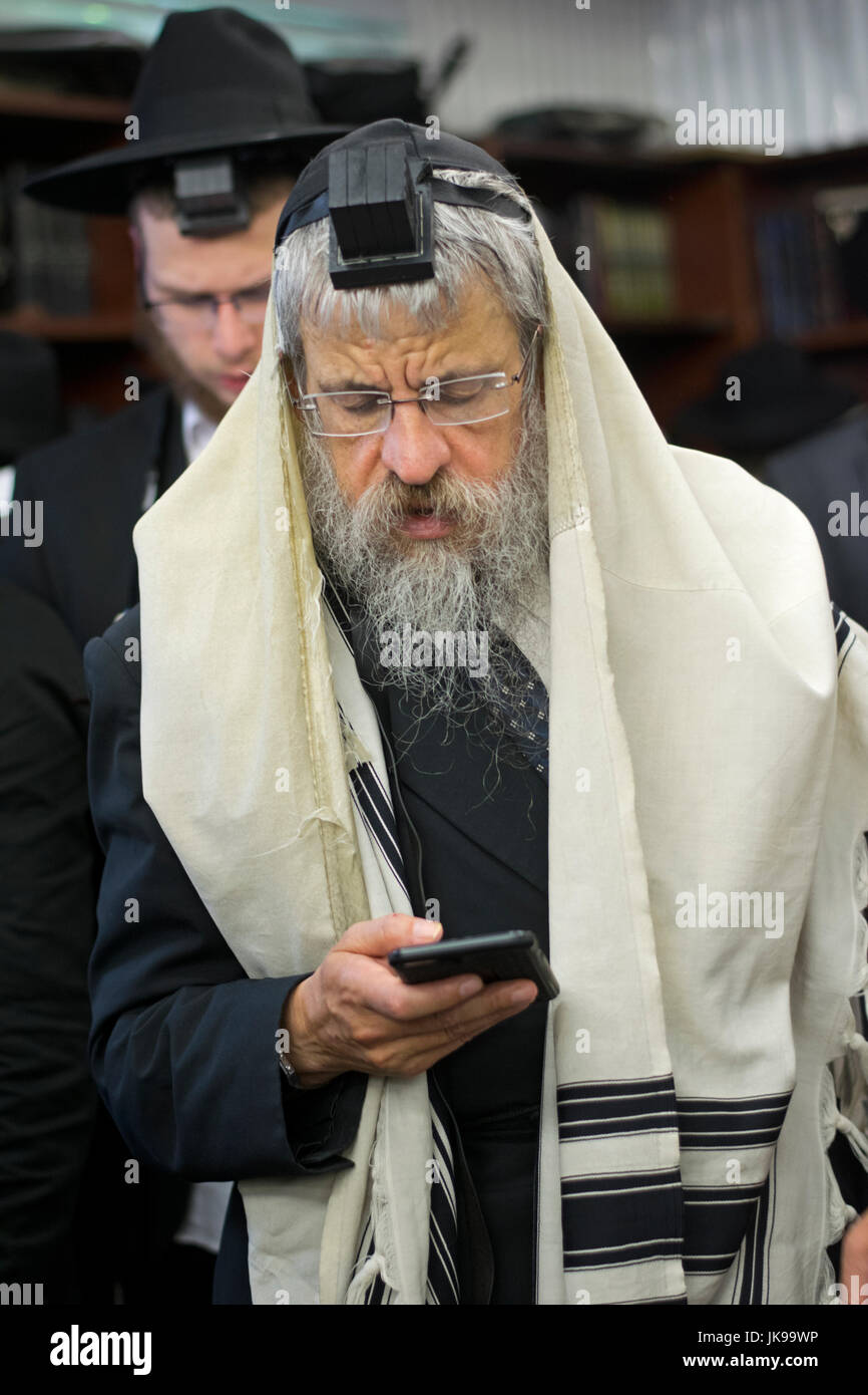 Un homme juif religieux récitant ses prières à partir d'un téléphone au lieu d'un livre de prières. Dans la région de Cambria Heights, dans le Queens, New York. Banque D'Images