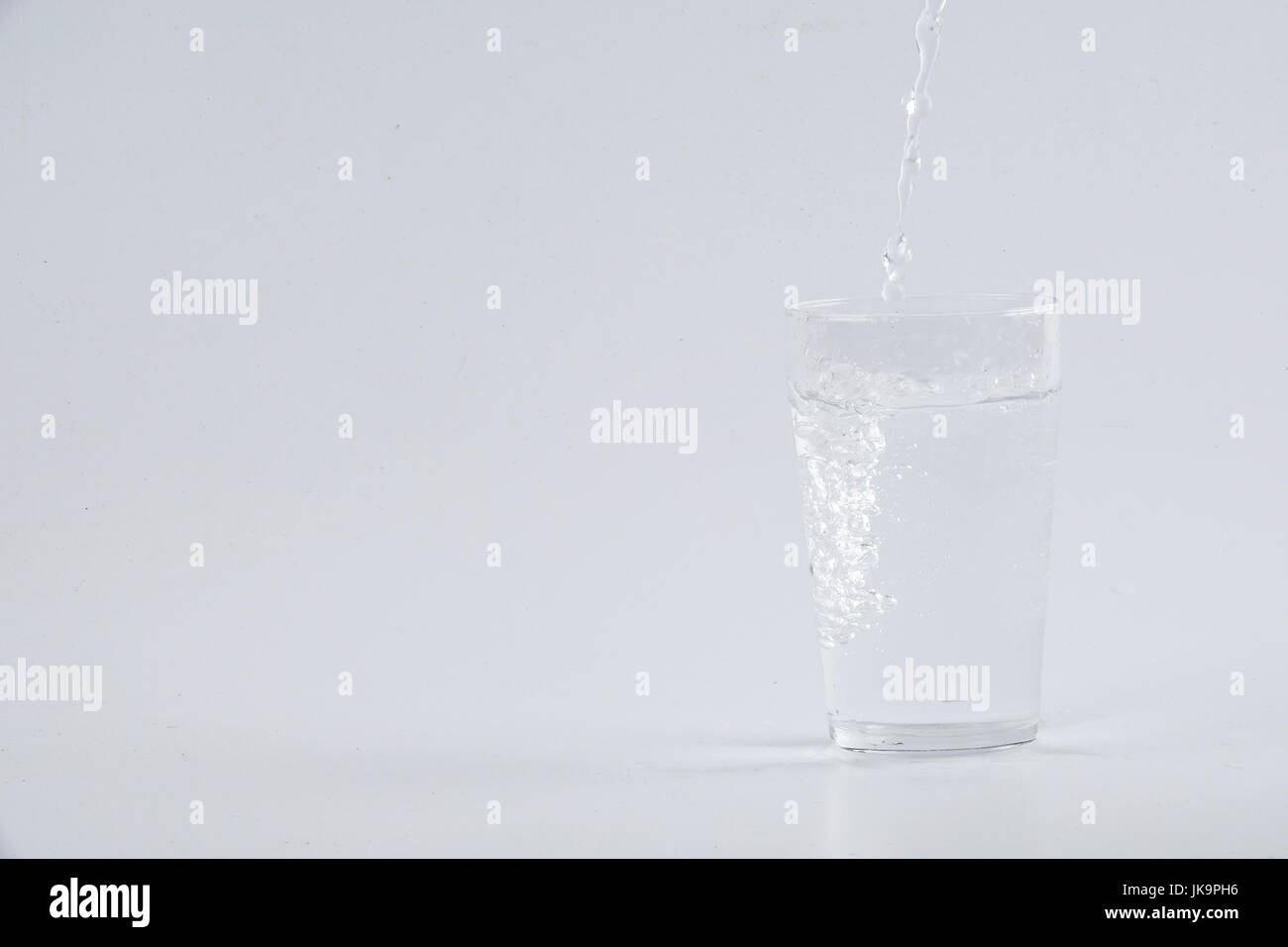 Verser de l'eau dans le verre clair sur fond blanc Banque D'Images
