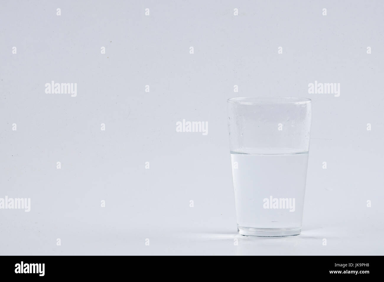 Verser de l'eau dans le verre clair sur fond blanc Banque D'Images