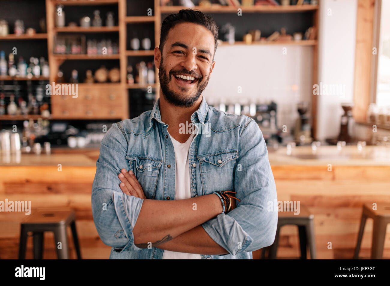 Portrait de jeune homme debout, les bras croisés dans un café. Smiling handsome guy standing dans un coffee shop. Banque D'Images