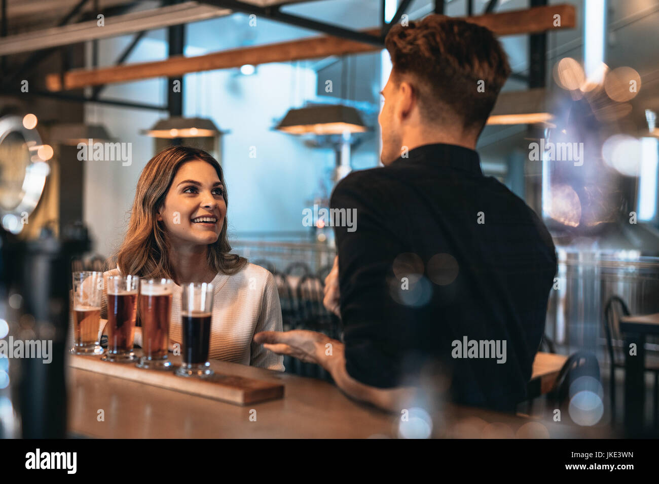 Jeune couple à bar avec bières artisanales différentes sur une table en bois. L'homme et la femme qui parle au bar comptoir. Banque D'Images