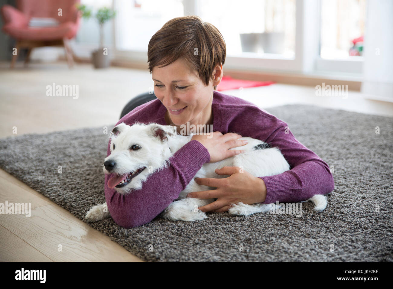 Femme couchée sur un tapis dans le salon hugging her dog Banque D'Images