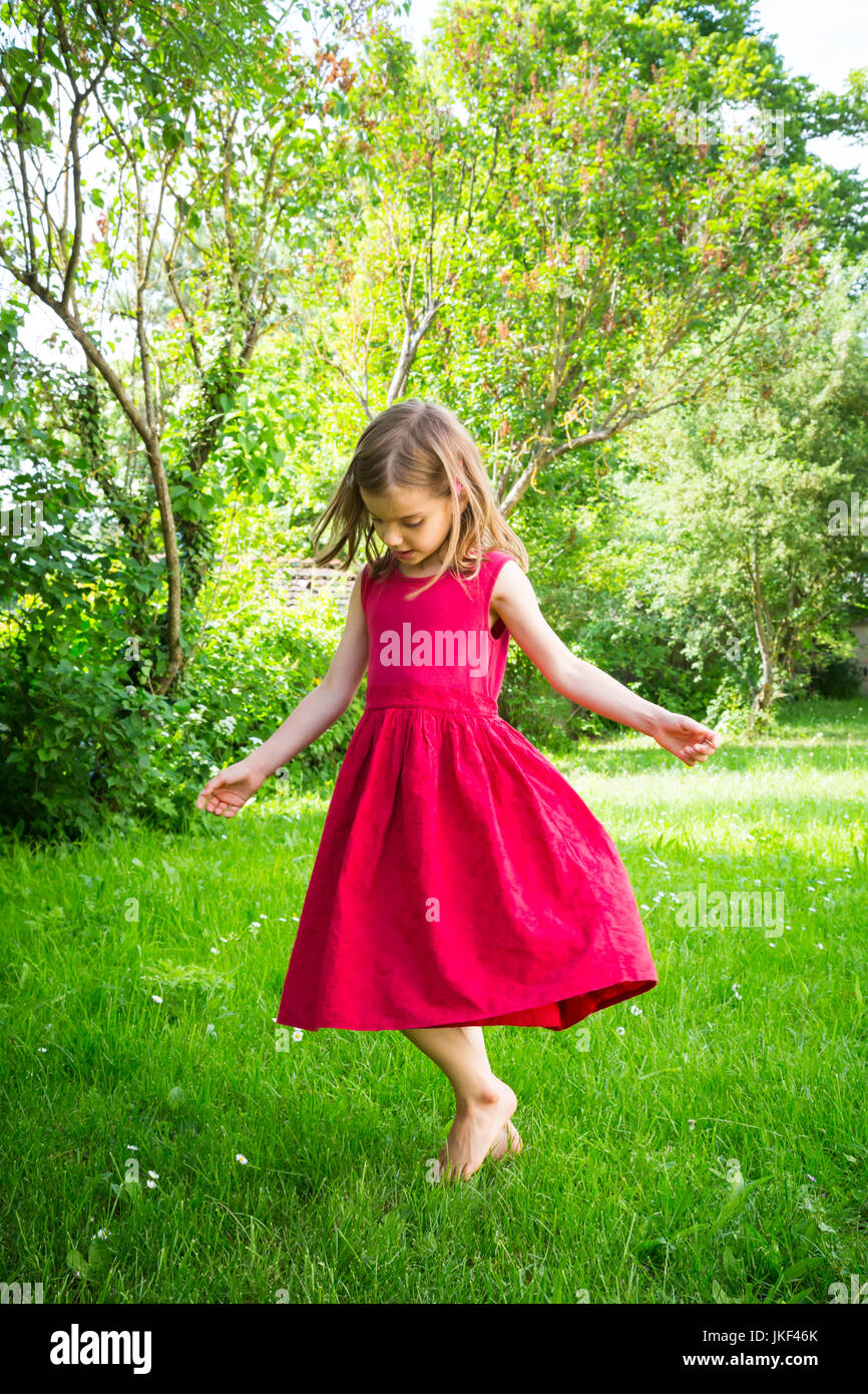 Little girl wearing robe rouge dansant sur un pré Banque D'Images