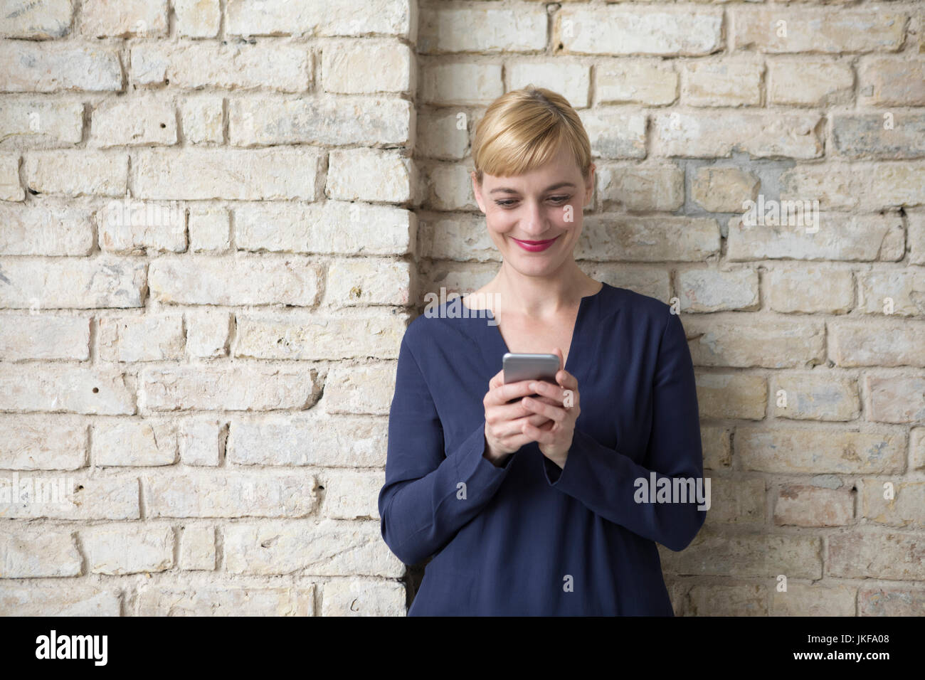Businesswoman leaning against brick wall, using smartphone Banque D'Images