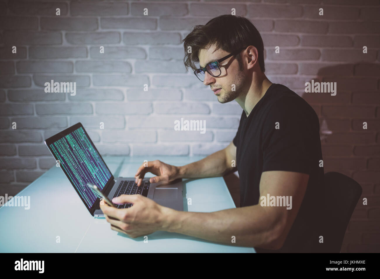 Beau jeune programmeur travailler en nuit avec logiciel et aussi utiliser le téléphone . Hacker Banque D'Images