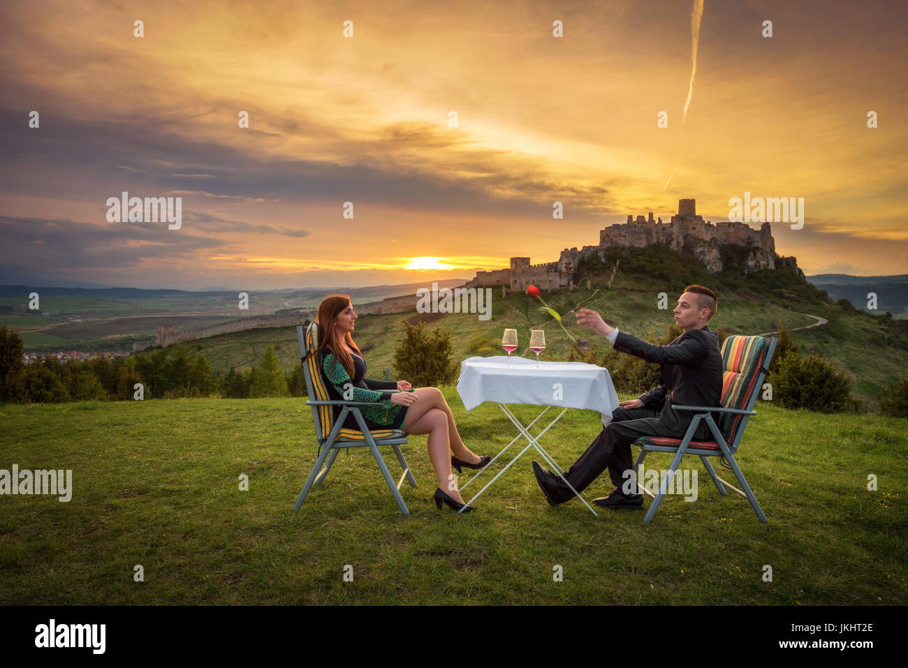 Couple in love boire du vin rouge dans la nature sous les ruines d'un château au coucher du soleil. Petit ami trows une tulipe à sa petite amie. Banque D'Images