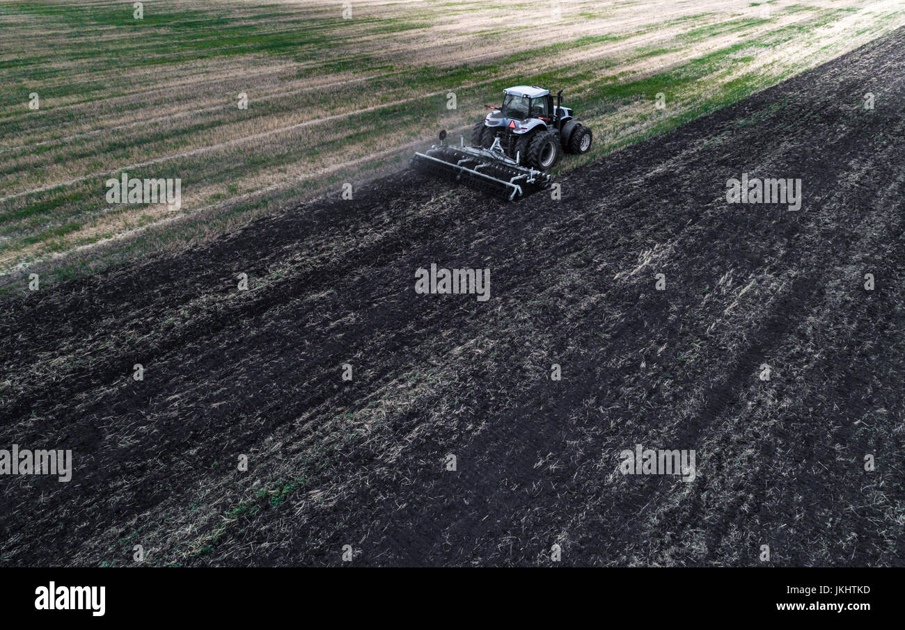 Le tracteur laboure le champ blanc sur fond de la terre noire, et derrière elle des oiseaux volent et la collecte de nourriture. Aeril vue. Machines agricoles Banque D'Images