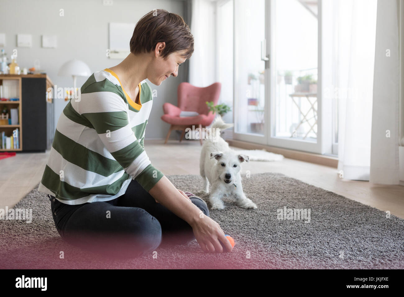 Femme assise sur le sol à la maison en jouant avec son chien Banque D'Images