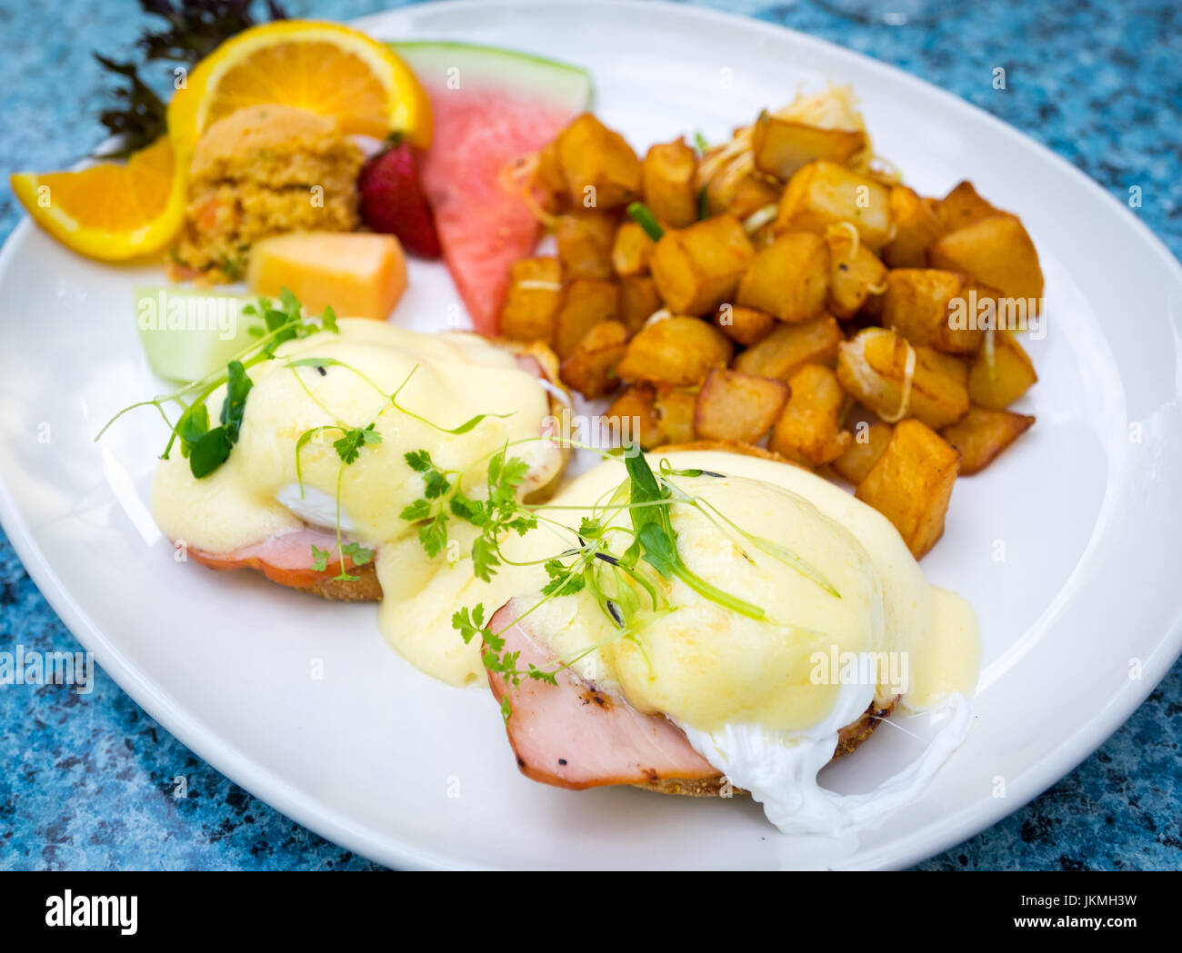 Oeufs Bénédictine classique (soft œufs pochés, Canadian bacon de dos, et sauce hollandaise sur un muffin anglais), frites, et des fruits pour le petit déjeuner. Banque D'Images