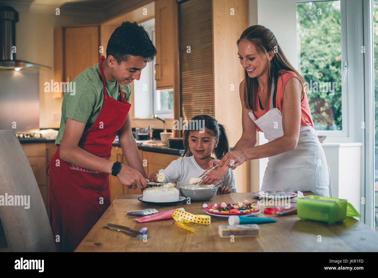 La décoration d'une mère gâteau avec son fils et sa fille dans la cuisine de leur maison. Ils couvrent le gâteau avec du glaçage et d'avoir des sucreries à décorer. Banque D'Images