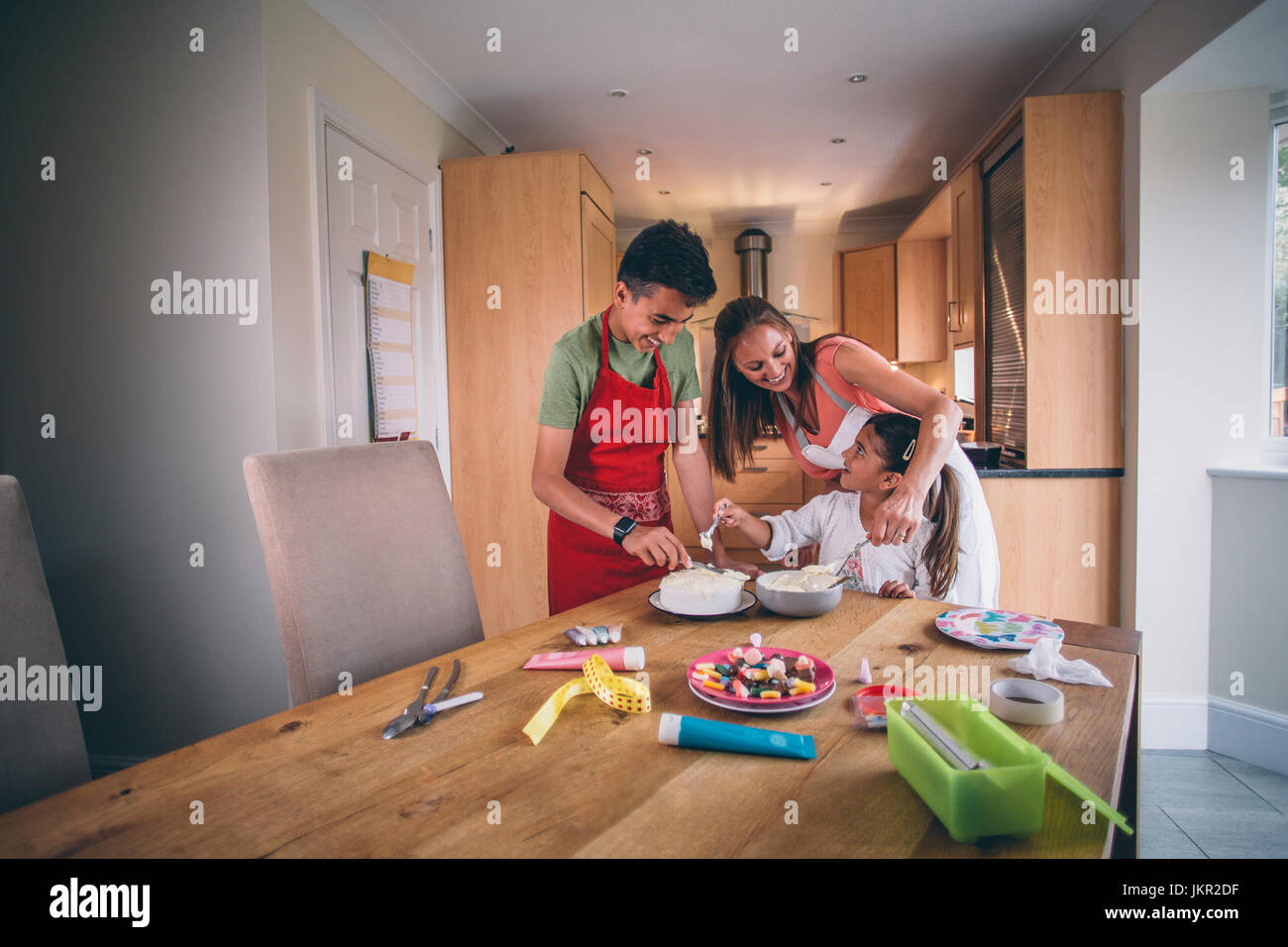 Mère d'aider son fils et sa fille pour décorer un gâteau dans la cuisine de leur maison. Banque D'Images