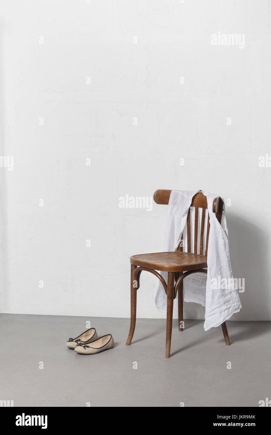 Tissu sur chaise en bois par ses chaussures contre le mur blanc Banque D'Images