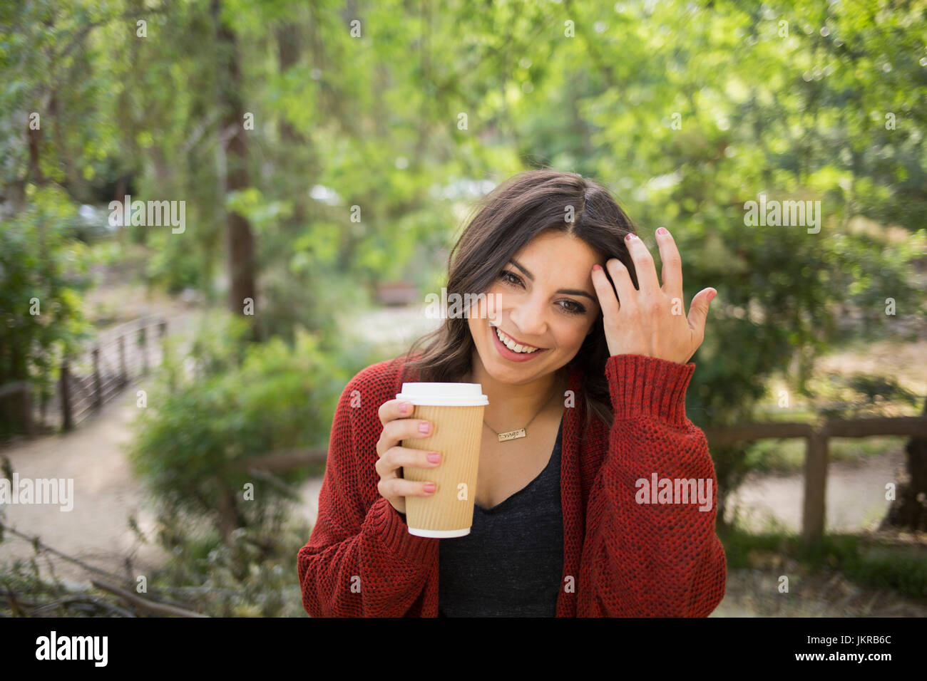 Cheerful woman holding glass jetables dans park Banque D'Images