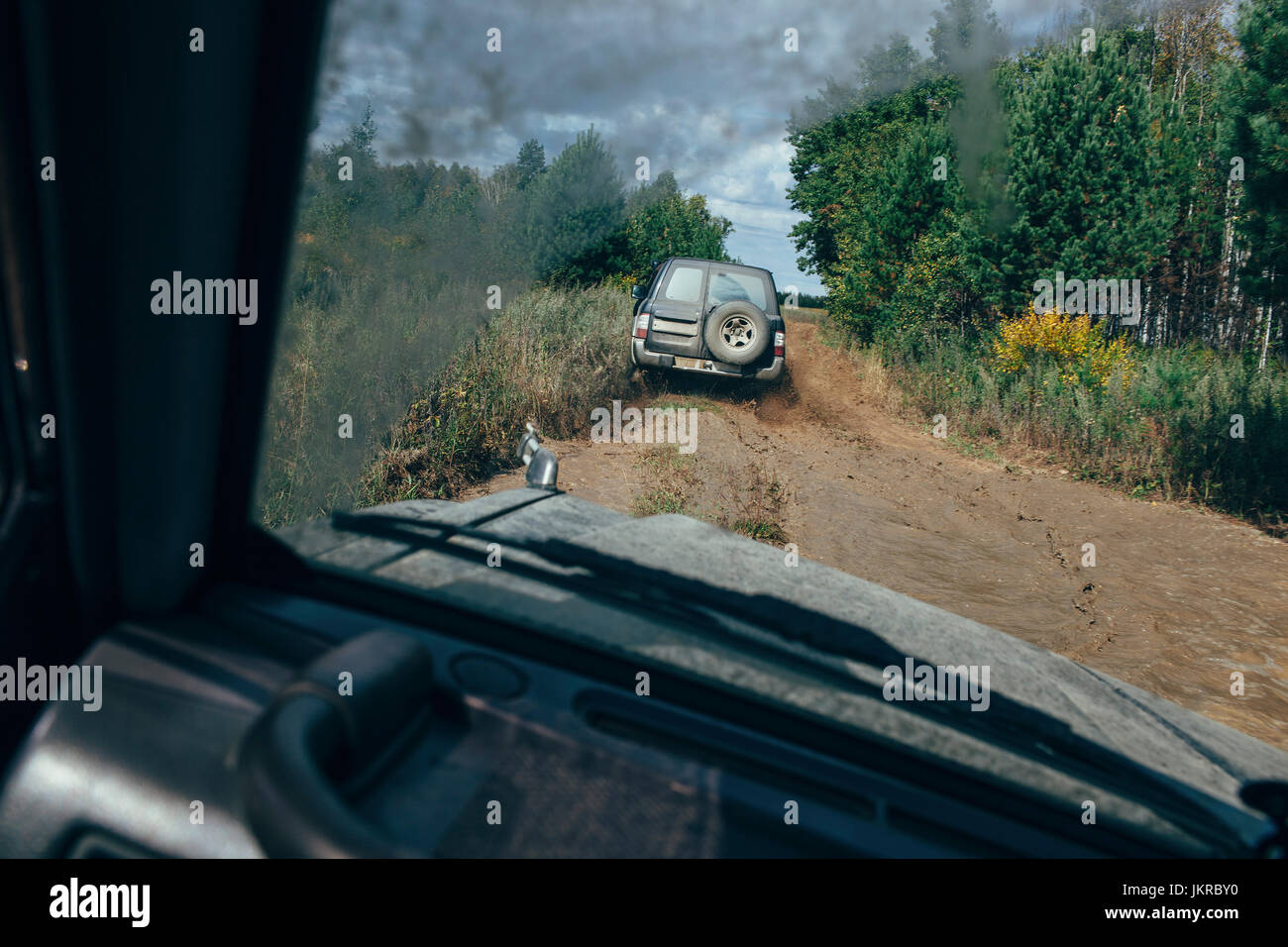 Véhicule hors route déménagement sur chemin de terre au milieu d'arbres vu à travers le pare-brise contre le ciel Banque D'Images