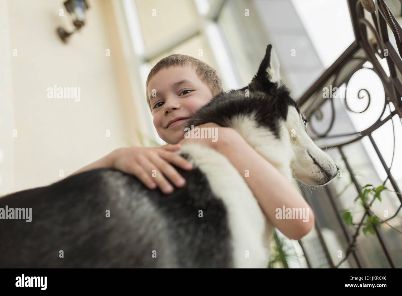 Low angle portrait of boy embracing dog by railing at home Banque D'Images
