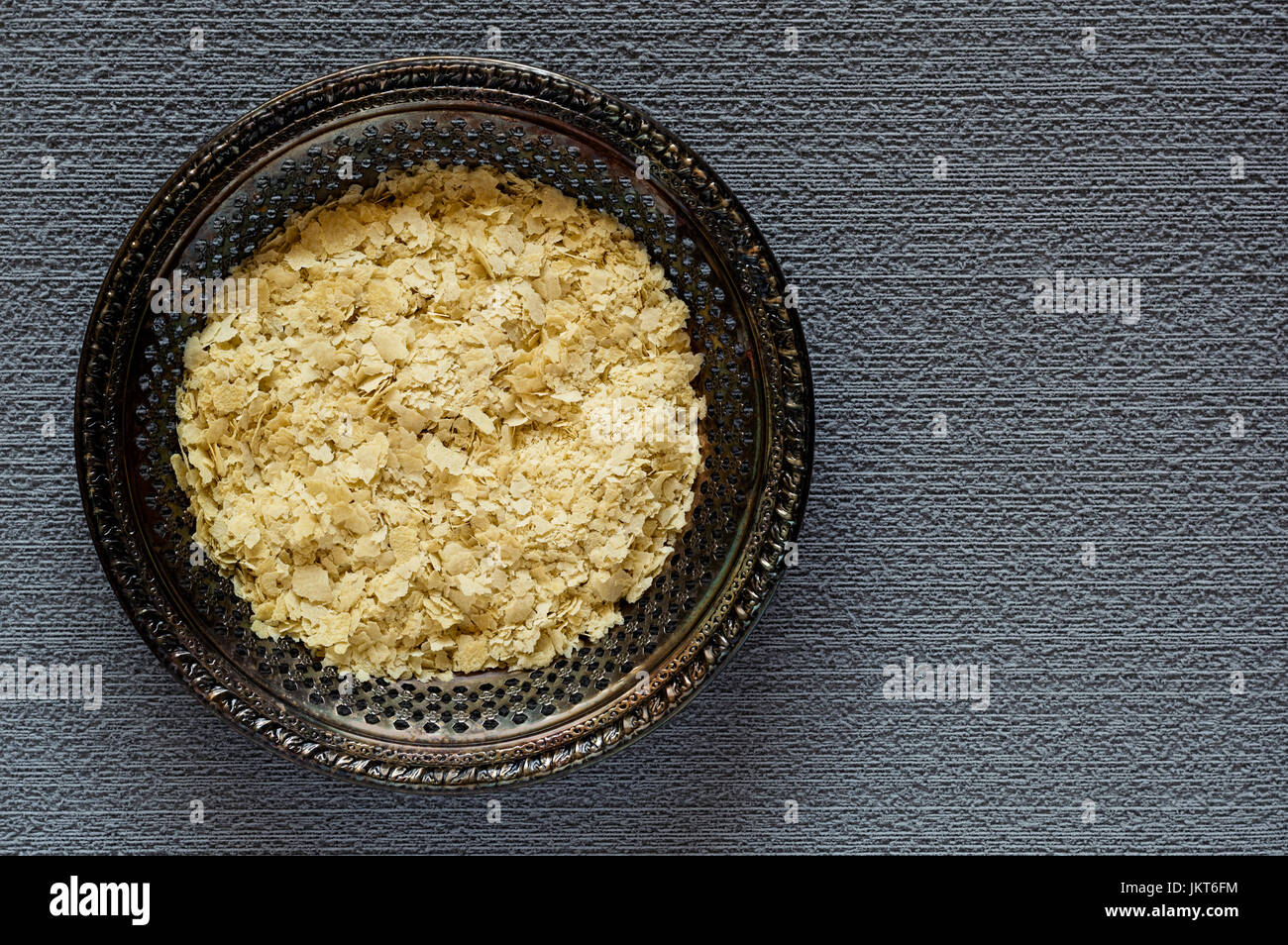 Vue de dessus de flocons de levure alimentaire séché sur une plaque de métal vintage sur un fond texturé, gris Banque D'Images