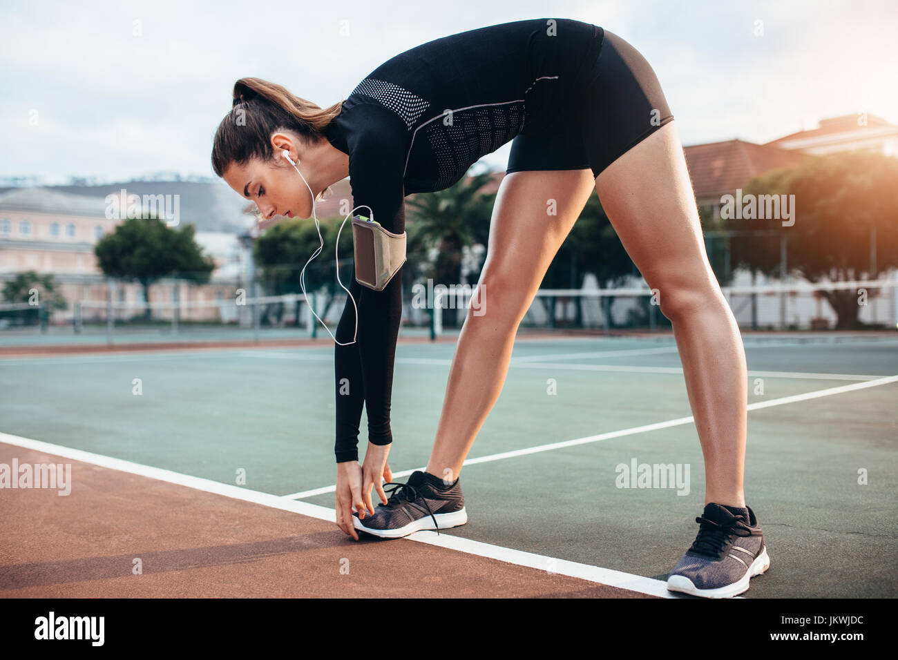 Beautiful young girl doing stretching workout extérieur. Grande sportive faisant l'exercice d'échauffement sur un court de tennis. Banque D'Images