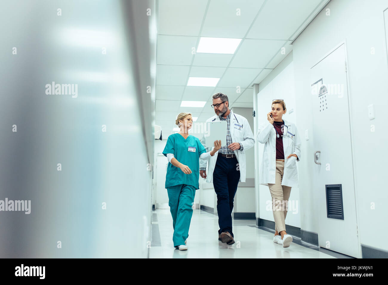 Groupe de medecins avec presse-papiers discutant le long couloir de l'hôpital. Médecin et l'infirmière rapport médical d'information avec des collègue talking on mobile ph Banque D'Images