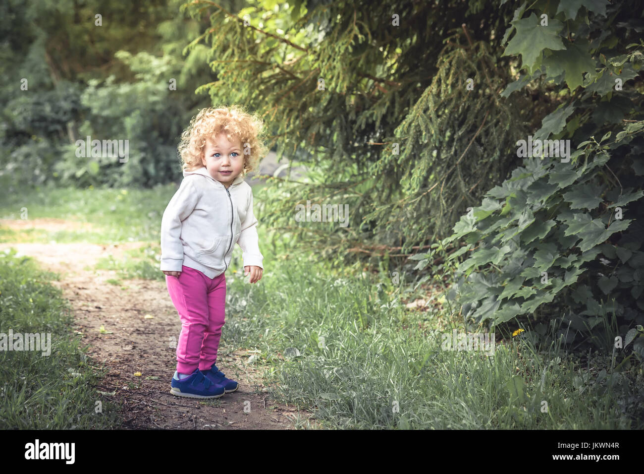 Cute girl enfant bouclés de marcher seul dans une forêt située sur le sentier entre les arbres pendant les vacances d'enfance insouciante heureux symbolisant Banque D'Images