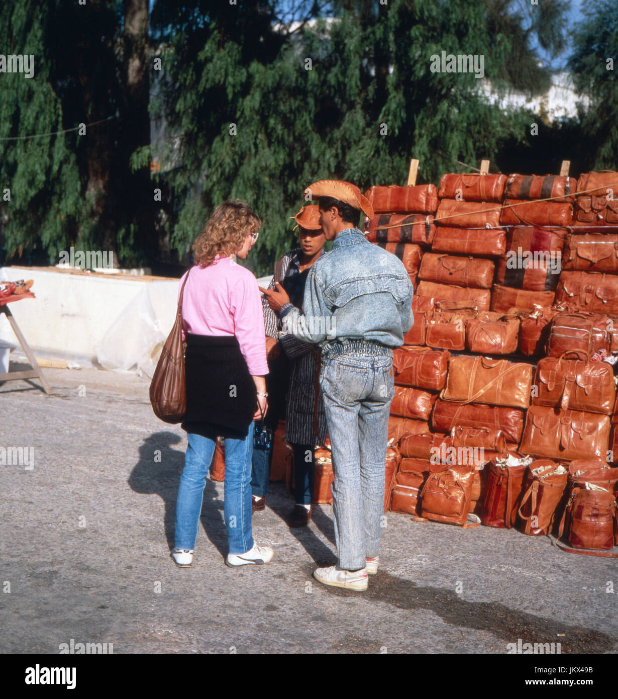 Eine Touristin feilscht mit einem Lederwarenhändler um den Preis à Sidi Bou Said, Tunesien 1980er Jahre. Une femelle avec un fournisseur négociation touristique d'articles en cuir à Sidi Bou Saïd, la Tunisie des années 80. Banque D'Images