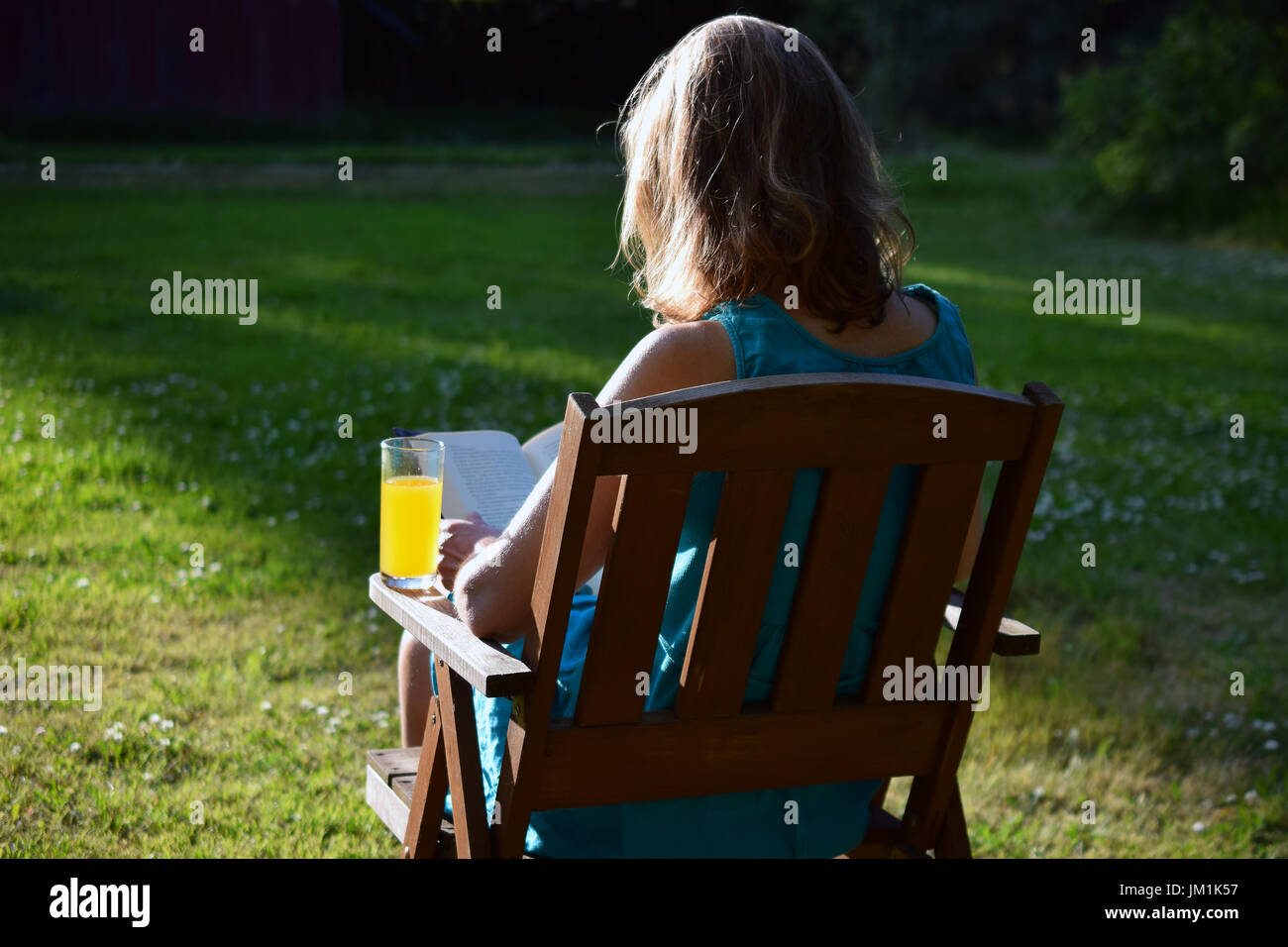 Woman Reading a book et jaune verre dans un jardin aux derniers rayons de soleil du soir sur l'été. Banque D'Images