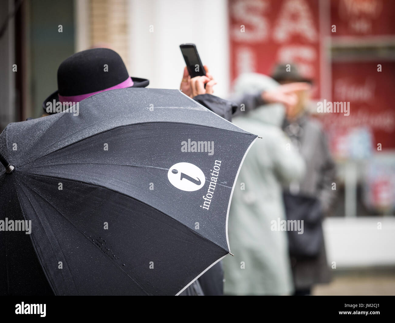 Informations touristiques sur parapluie - un guide touristique Cambridge vérifie son téléphone sous la pluie dans le centre de Cambridge UK Banque D'Images