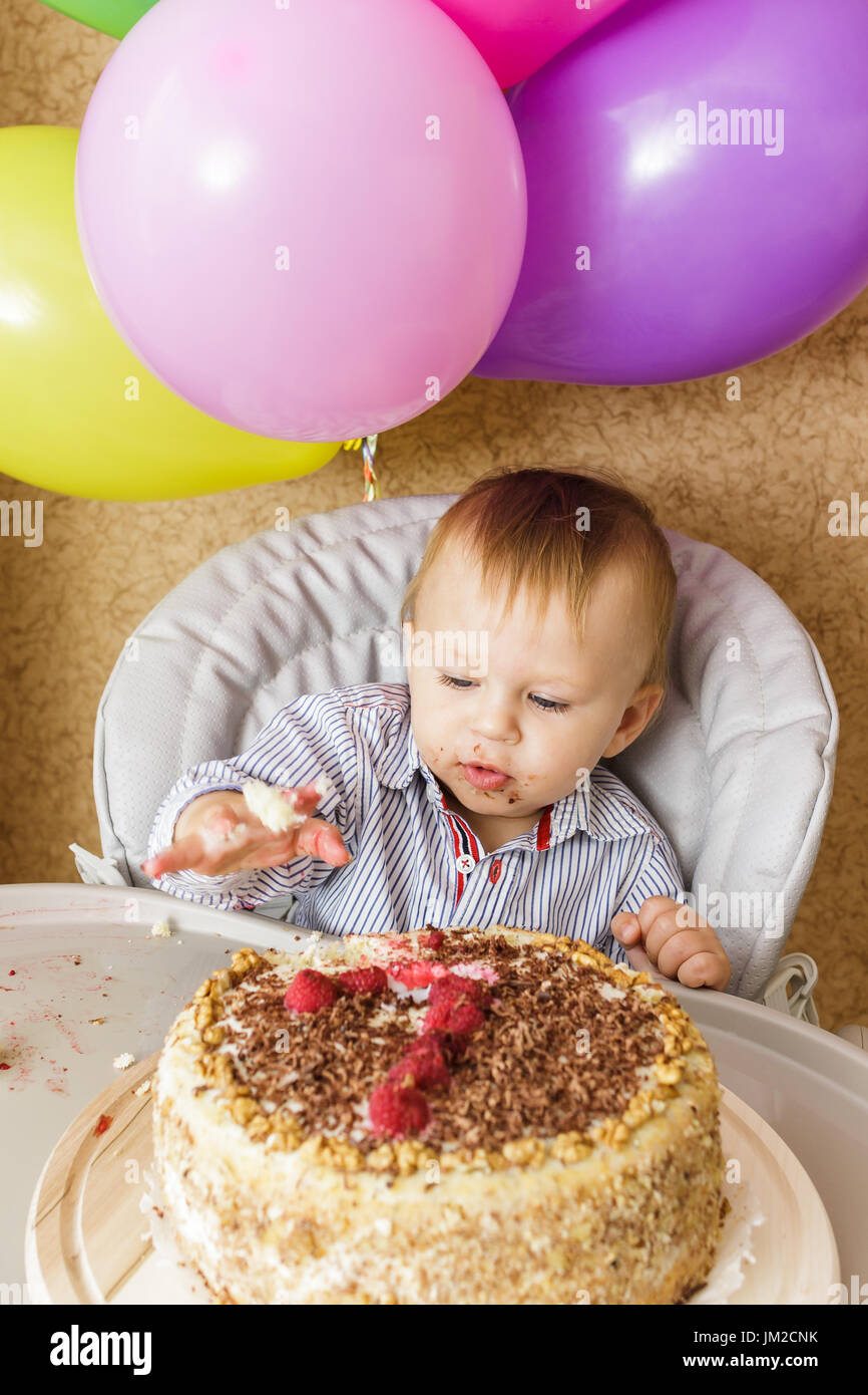 Un petit garçon est assis dans une chaise haute et sa dégustation de gâteau. Premier Anniversaire Célébration de concept. Smash gâteau Banque D'Images