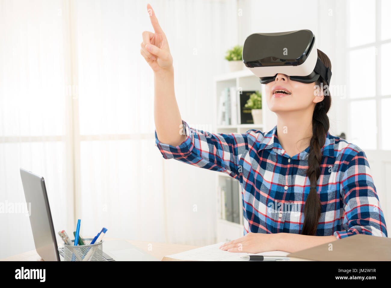 Jeune femme confiante dans casque de réalité virtuelle à l'aide de technologies de pointe dans le VR tout en l'air assis à sa place de travail bureau. Banque D'Images