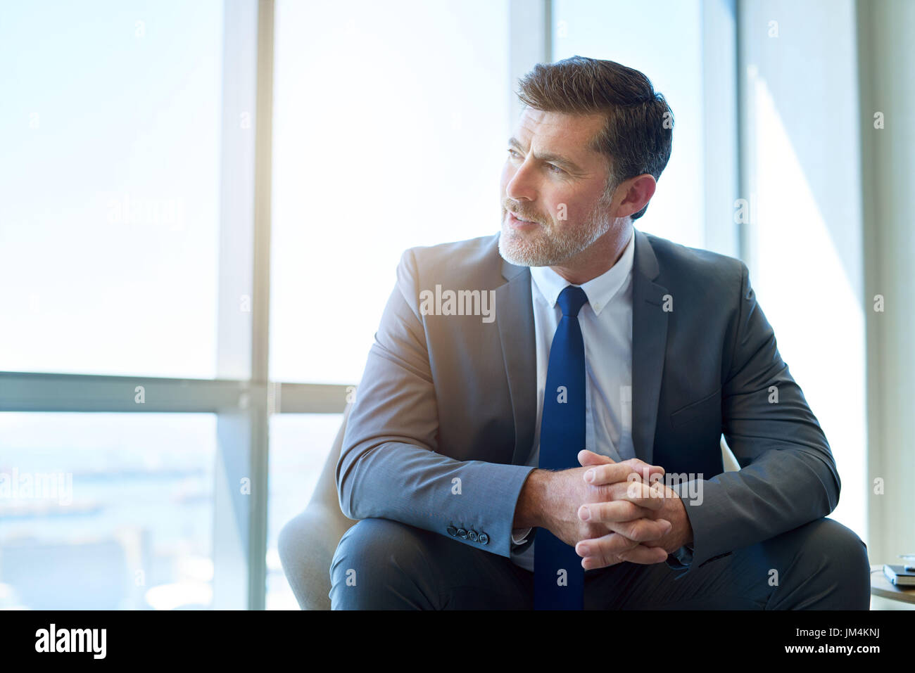 La maturité d'affaires et un entrepreneur assis dans un espace de bureau moderne avec de grandes fenêtres, à l'écart avec une attitude positive et optimiste express Banque D'Images