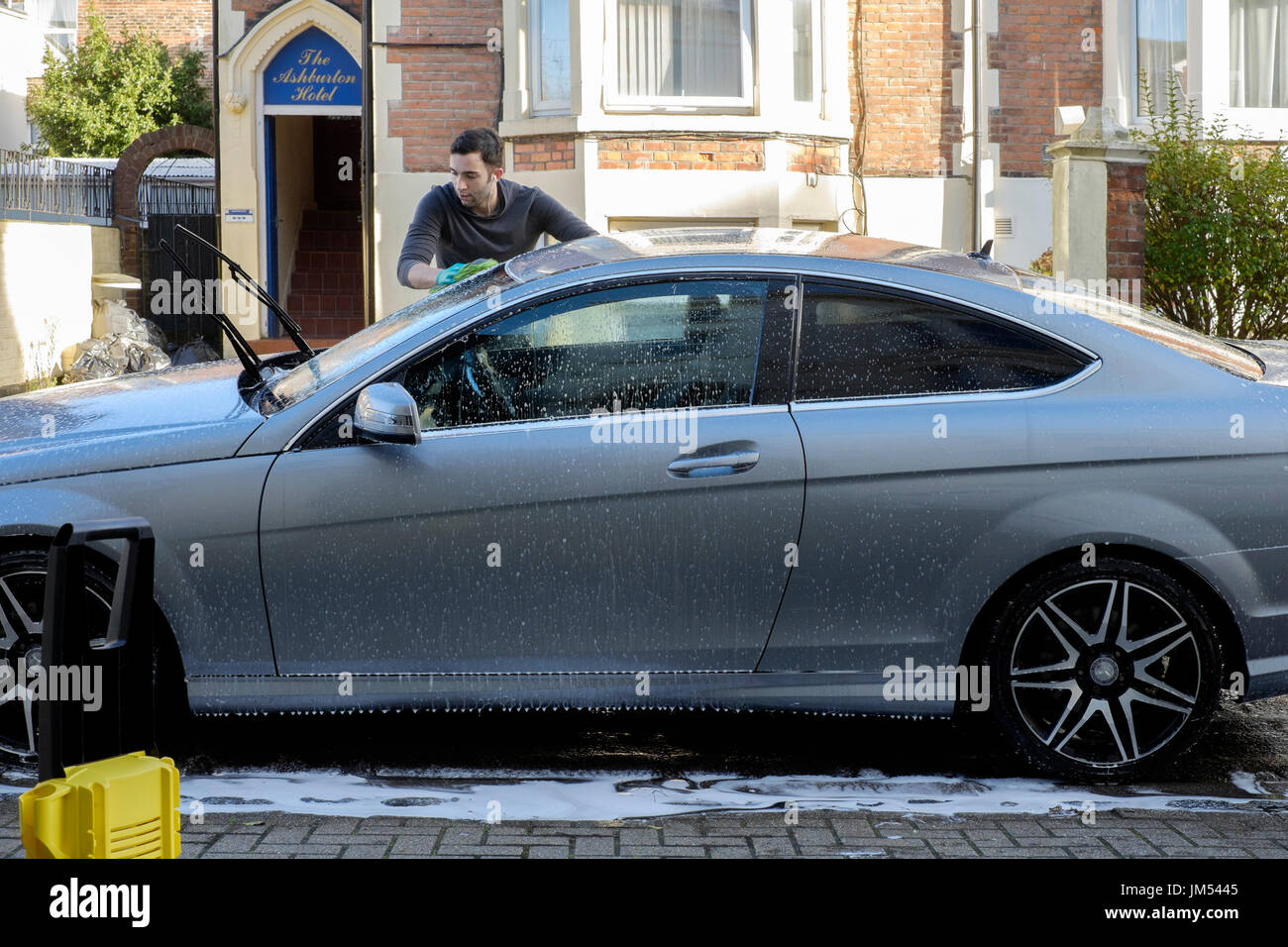Jeune homme nettoyant sa voiture avec la rondelle de pression et l'éponge england uk Banque D'Images