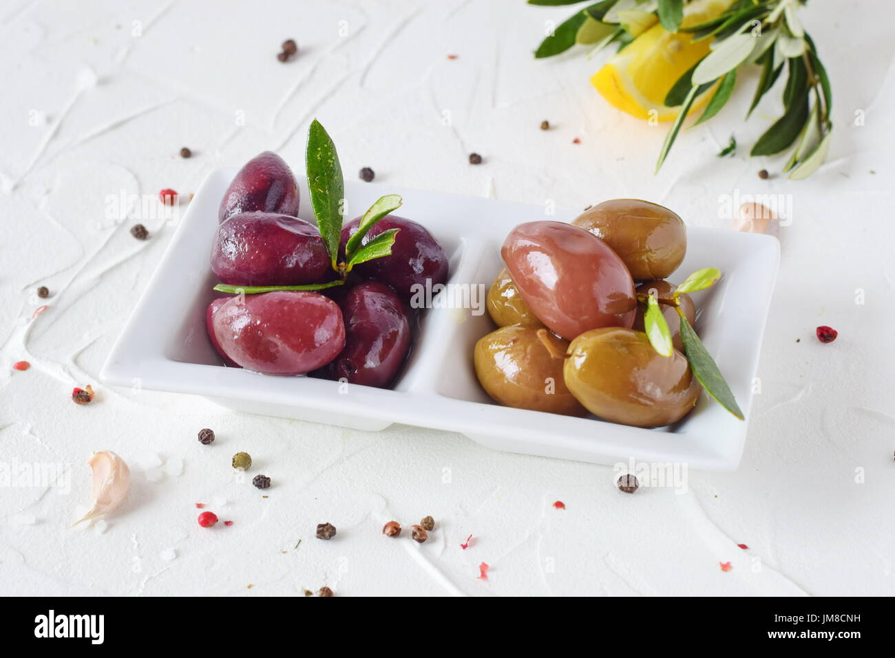Plaque blanche avec olives vertes et noires avec feuilles d'olivier sur un fond abstrait blanc avec du citron, tomate cerise, d'épices. Alimentation saine. La nourriture grecque. La cuisine méditerranéenne. Banque D'Images