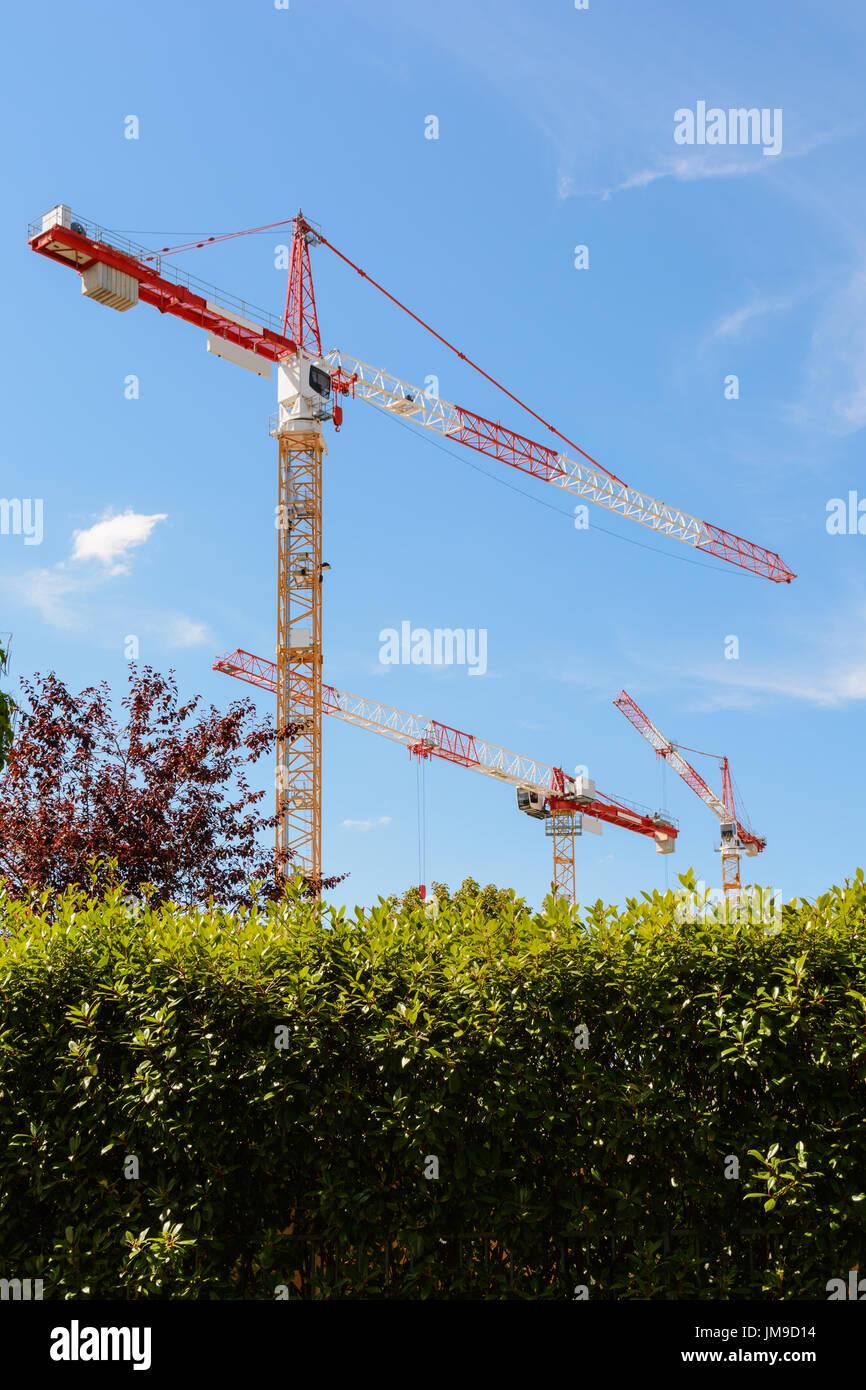 Low angle view of trois grues à tour sur un chantier avec le feuillage sur fond de ciel bleu. Banque D'Images