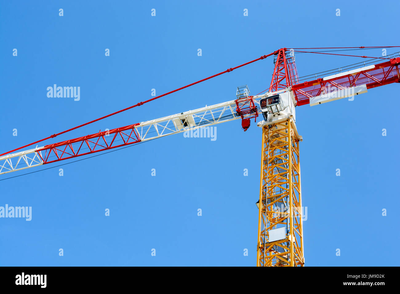 Low angle view of a grue a tour à tour jaune et une flèche rouge et blanche et de la contre-flèche articles contre le ciel bleu. Banque D'Images