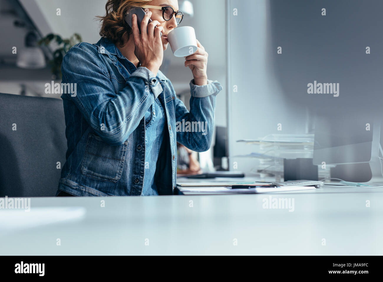 Femme au travail à boire du café et conversation sur téléphone mobile. Young businesswoman at work making phone call et le café. Banque D'Images