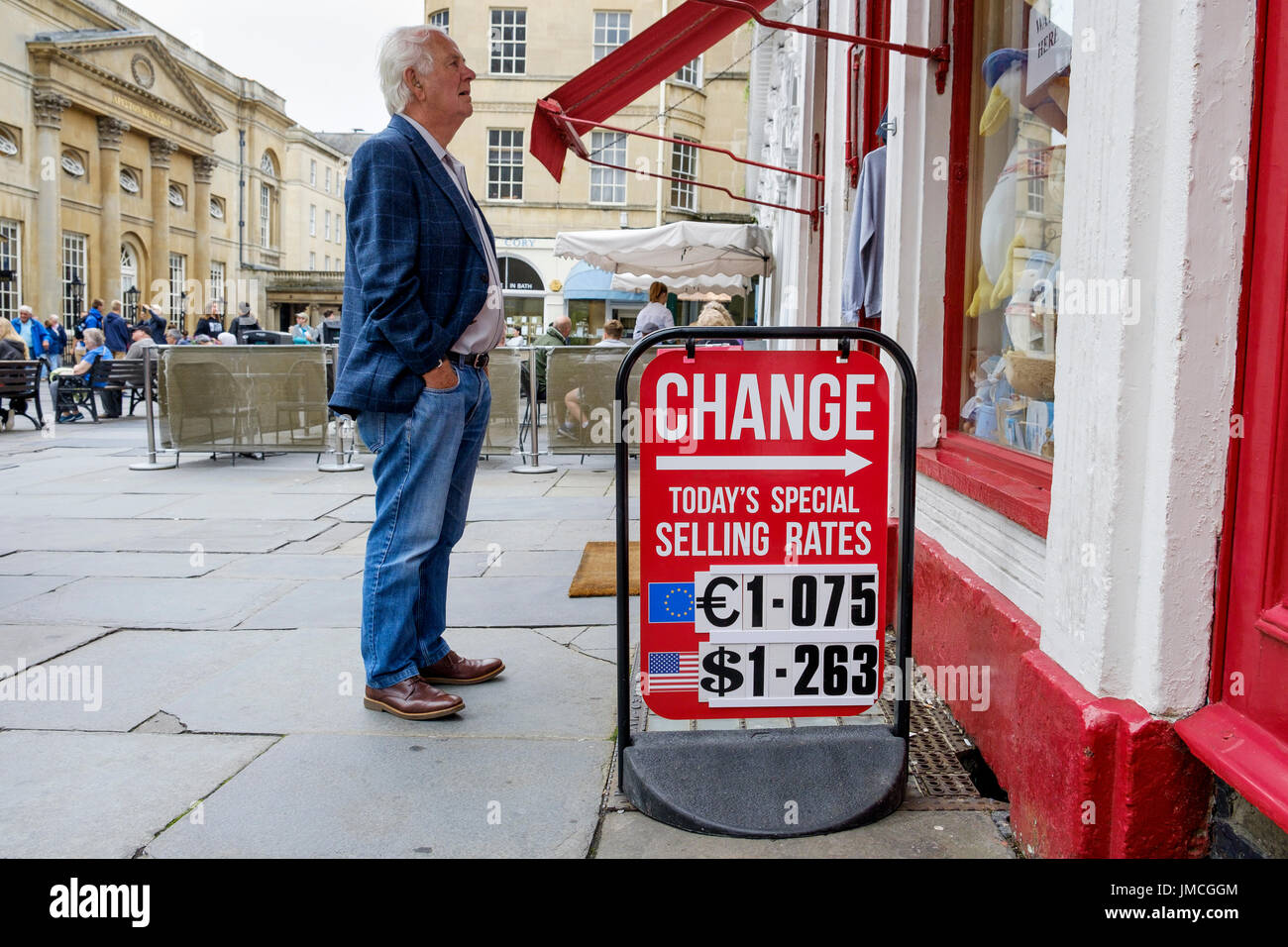 Un homme debout à côté d'une carte d'affichage du taux de change est représenté à la recherche dans un des bureaux de change situés dans une boutique touristique à Bath, Angleterre Banque D'Images