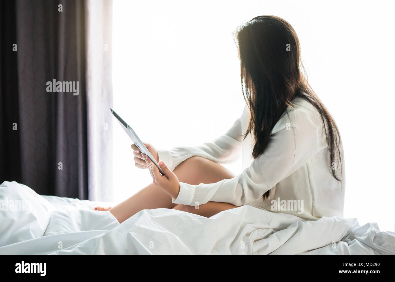 Asian woman utiliser une tablette sur le lit après service de week-end en mornning.Utiliser la tablette pour lire les nouvelles, regarder des films, ou en chat, Communications et relations extérieures Banque D'Images