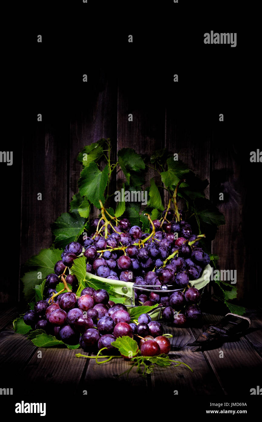 Les raisins rouges frais bouquet allongé sur feuilles sur une vieille table en bois. Photographié avec technique de peinture lumière Banque D'Images