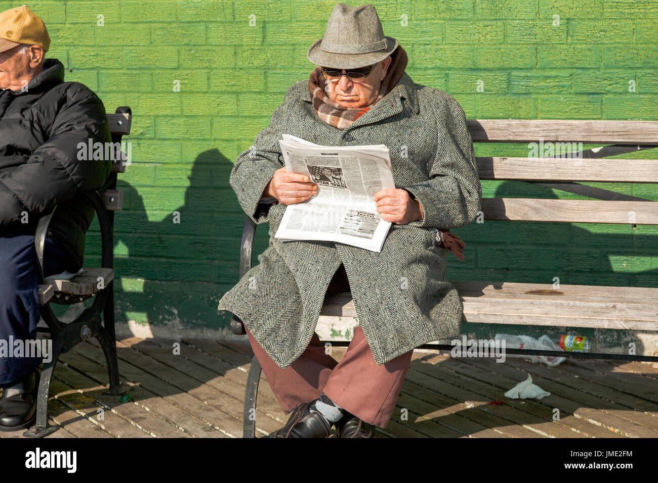 Un homme dans un manteau et un chapeau lit un journal russe à Brighton  Beach, New York City. Il est assis sur un banc contre un mur végétal Photo  Stock - Alamy