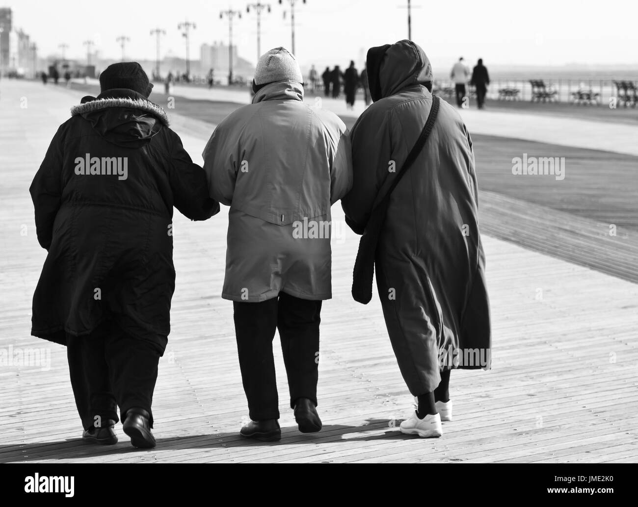 Trois femmes âgées amis de manteaux à marcher ensemble bras dessus bras dessous à l'extérieur en hiver. Noir et blanc. Vu de l'arrière. Banque D'Images