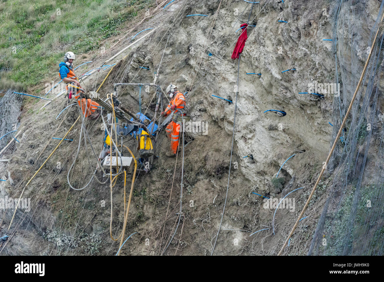 Prise téléphotographique ouvriers le perçage des trous pour les vis de stabilisation falaise rock & chutes subséquentes mesh. Rock International Day, le travail précaire concept Banque D'Images