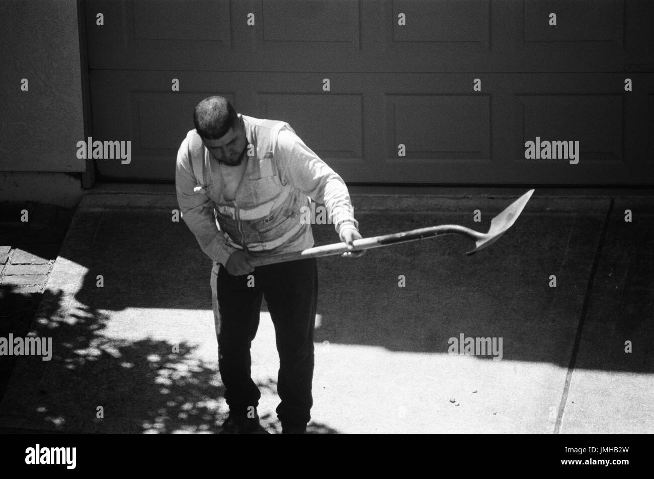 Un travailleur de la construction se plie dans le soleil chaud puisqu'il s'apprête à lever une charge d'asphalte avec une longue pelle, San Ramon, Californie, le 26 juin 2017. Banque D'Images