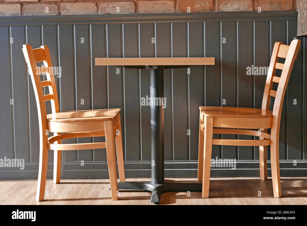 Table éclairée sur le côté et deux chaises en bois de couleur claire contre les murs lambrissés Banque D'Images