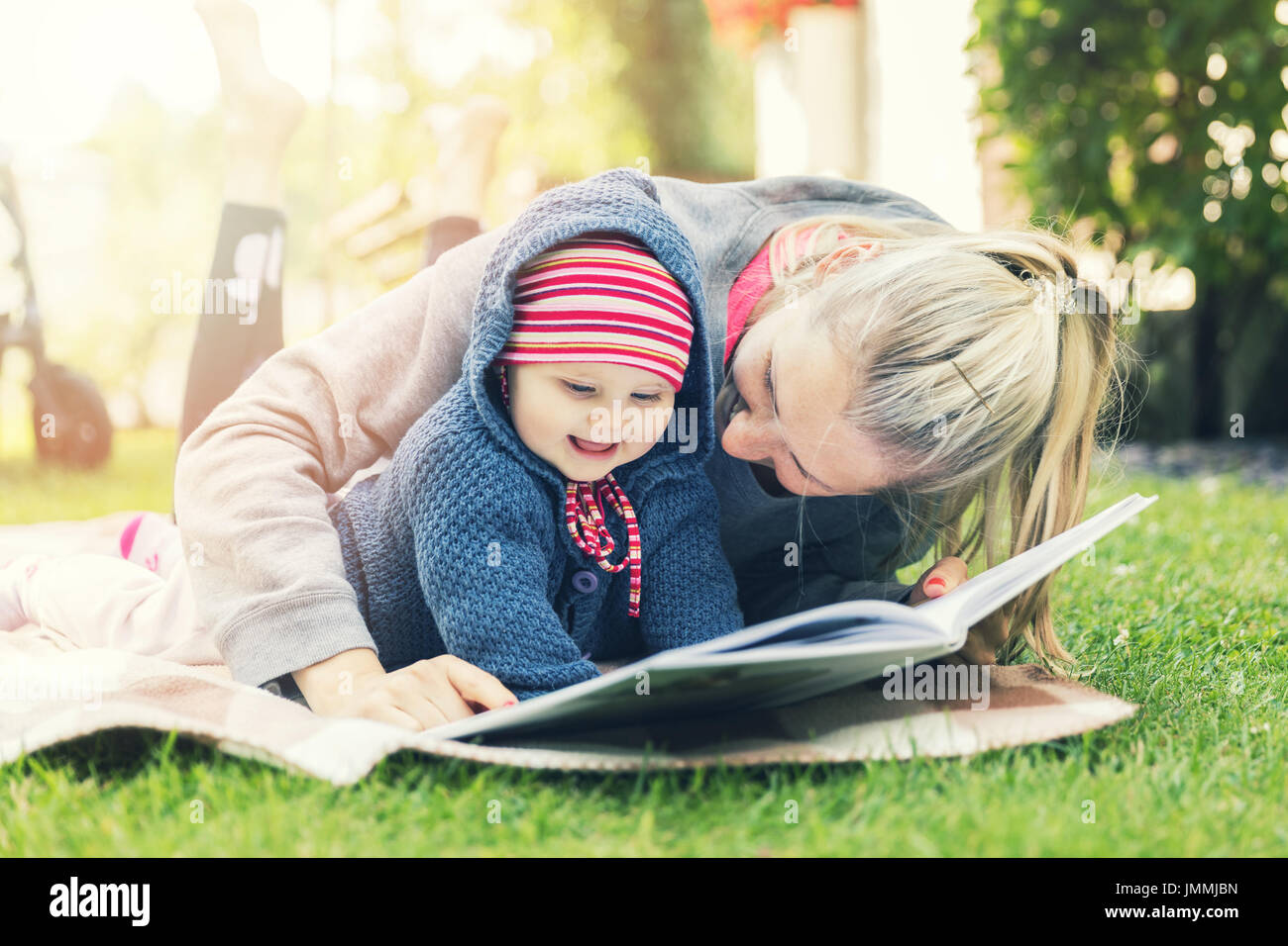Mère et little baby girl reading book together on blanket outdoors Banque D'Images