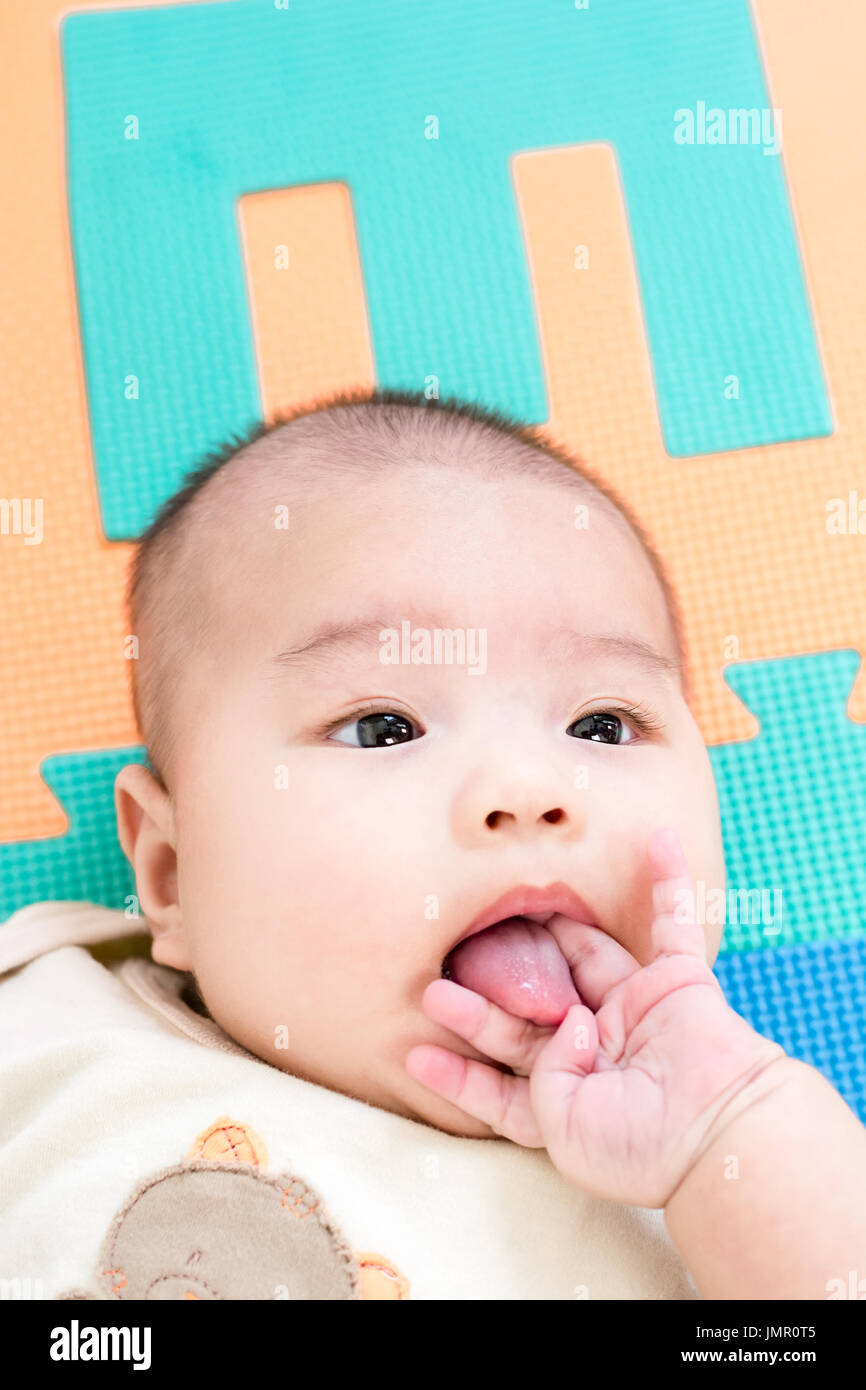 Portrait d'un adorable petit bébé fille bébé allongé sur le dos sur mousse eva colorés avec le doigt sur la bouche Banque D'Images