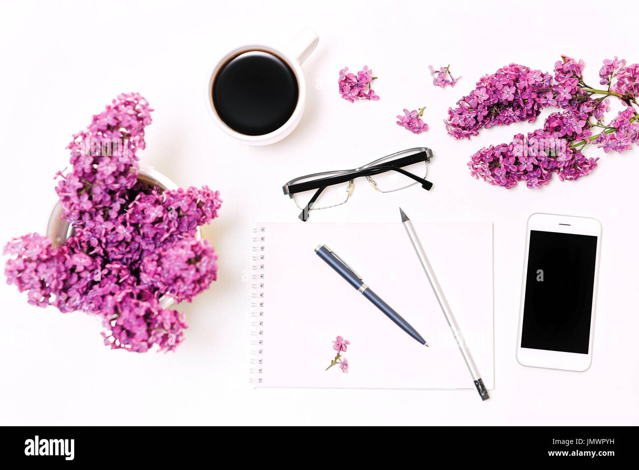 Lieu de travail avec téléphone mobile, ordinateur portable, stylo, crayon, verres et lilas fleurs sur l'arrière-plan du tableau blanc. Mise à plat, vue du dessus Banque D'Images
