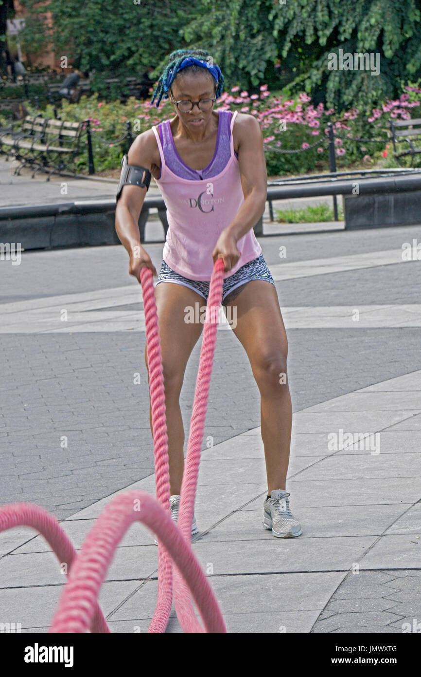 Une jolie jeune femme musculaire fit travailler dehors sur la bataille des cordes pendant un cours de conditionnement physique en plein air à Washington Square Park à Greenwich Village, Banque D'Images